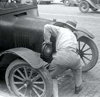 Photo of man bending down to crank start a vintage car, b/w