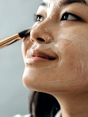 Photo closeup of a woman's face as she applies a cream over the skin with a brush