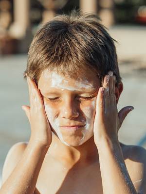 Photo of a boy using his hands to spread sunscreen on his face, upper body facing front