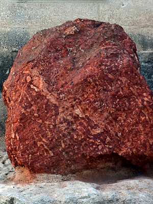 Photo of a red-brown, clay-like boulder of bauxite, part of a commemorative display