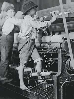 Photo of Victorian child labor shows small boy working while standing on frame of cotton textile factory machine