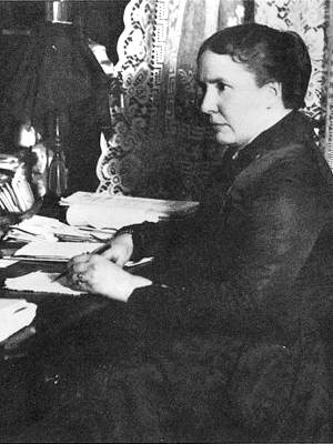 Photo Alice Cunningham Fletcher seated at her writing desk with pen and paperwork, upper body, facing left