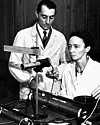 Thumbnail photograph of apparatus on a bench with Frederic and Irène Joliot Curie running their experiment
