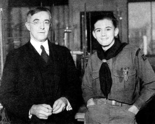 Dr. Irving Langmuir stands beside Lee Brown in Boy Scout uniform, upper bodies facing forward, laboratory in background