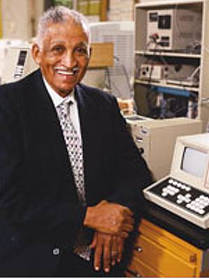 Photo of Samuel Massie leaning on a chemistry lab bench with electronic instruments in the background