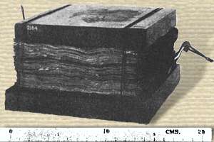 Photo of a stack of thin metal plates, bound between wood blocks top and bottom. About 15 cm square x 10 cm high. 