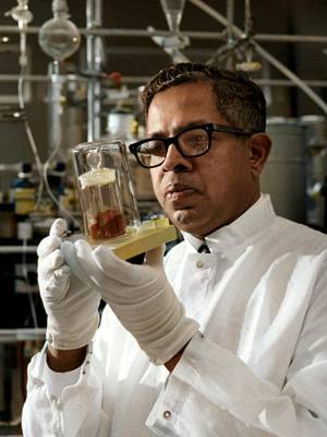 Colorized photo Cyril Ponnamperuma in lab coat, in lab, upper body, facing half-right, glass container held up to view closely