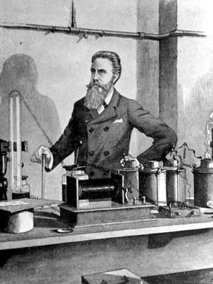 Sketch of Röntgen standing behind lab bench with apparatus including large magnetic coil, capacitors and wires