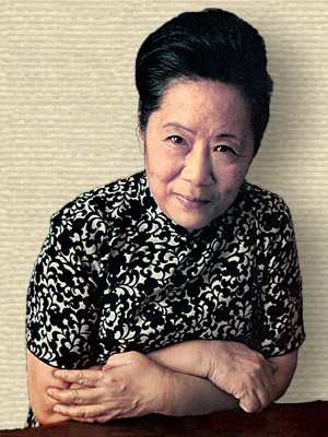 Photo of Chien-Shiung Wu, upper body, facing forward, arms folded leaning on table top.